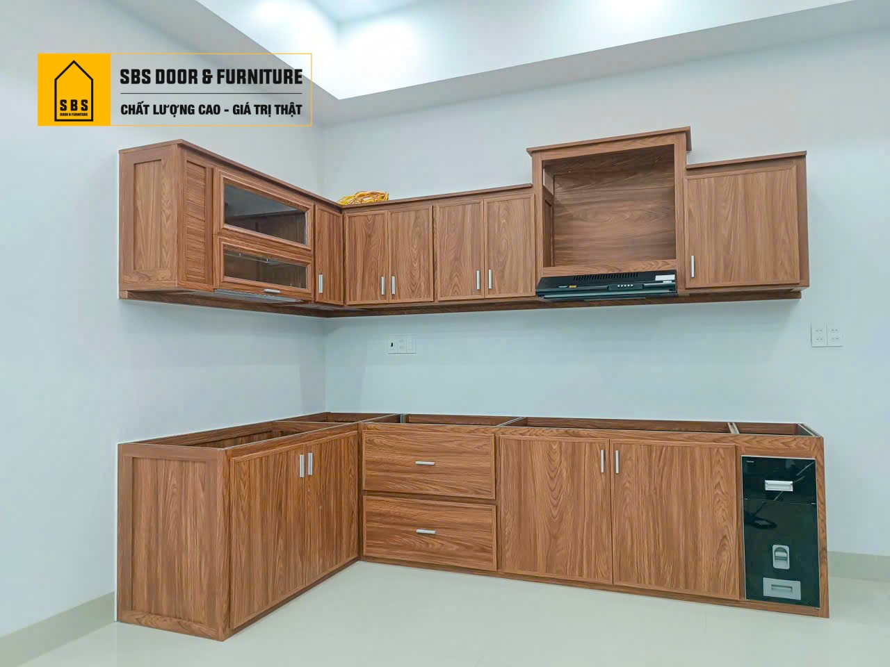 Mẫu tủ bếp chữ L với vân gỗ, thiết kế gọn gàng, tiết kiệm diện tích mà vẫn đầy đủ công năng.